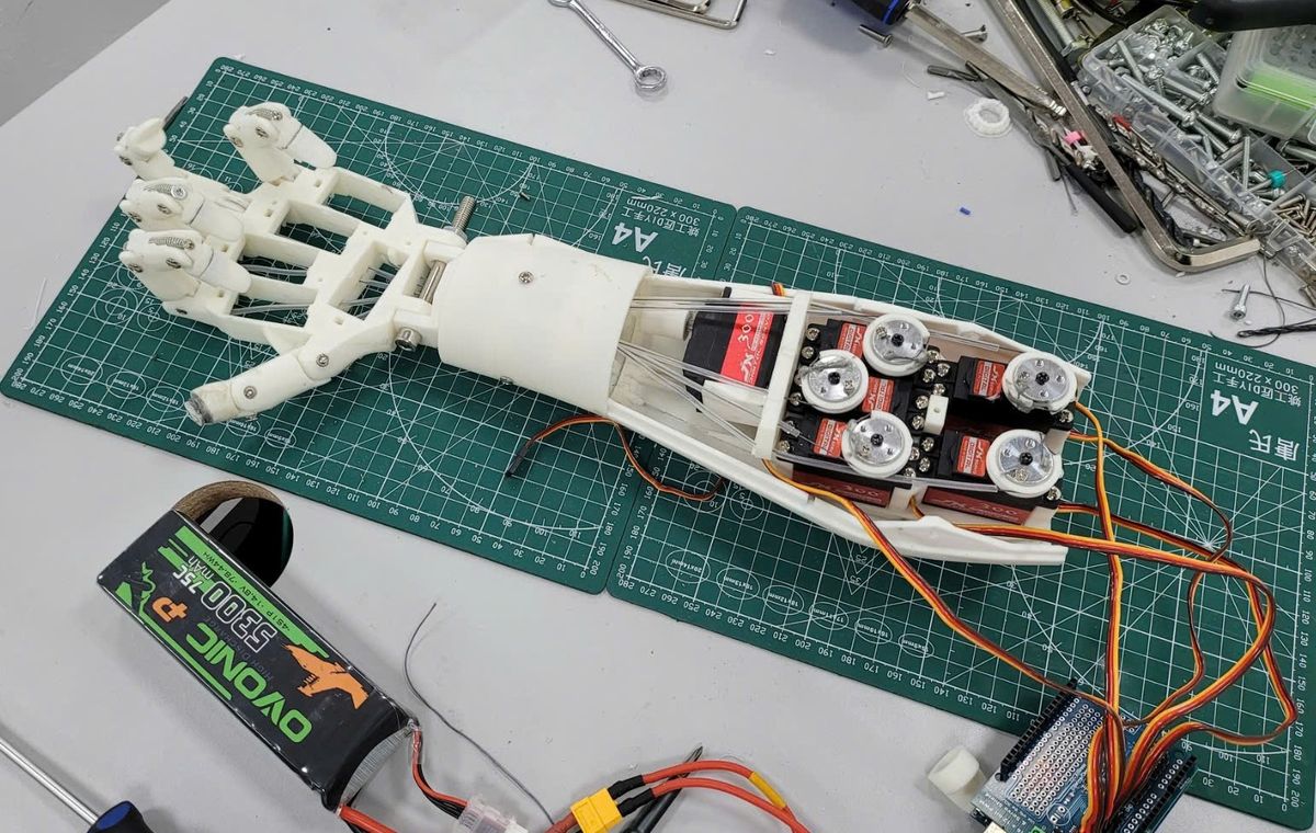 The open forearm and hand on a cutting mat: a row of servos with pulley wheels inside the forearm, and leads running out to a test board.