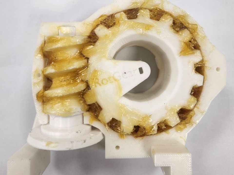 A printed shoulder gearbox, open: a worm on the left meshing with a large toothed wheel, both coated in grease.