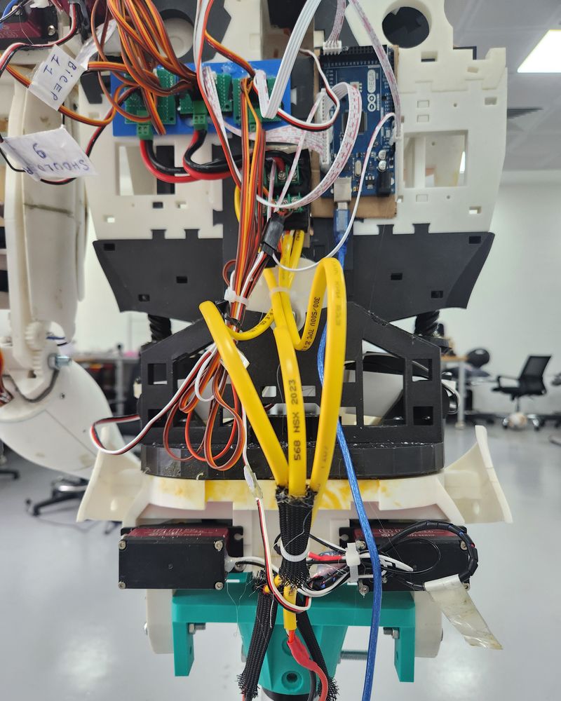 The robot's back: an Arduino Mega and green servo driver boards at the top, with bundles of servo leads and thick power cables running down to the base.