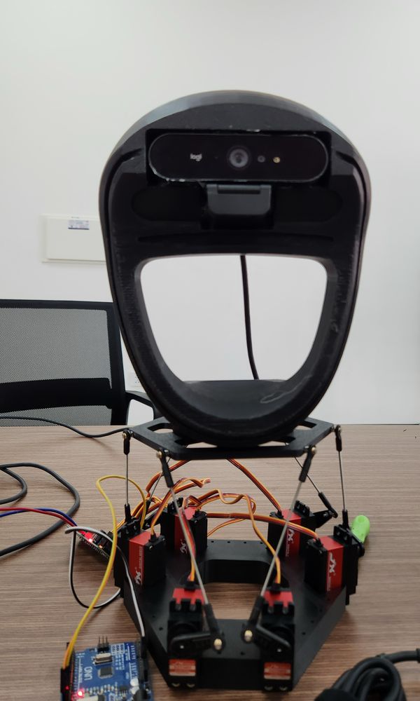 The neck from the front: a black 3D-printed head with a webcam in its forehead, on a small top plate held by six rods from six red servos on a hexagonal base.