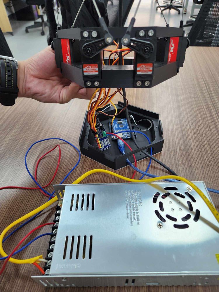 A hand lifts the servo plate above the base; in front lies the metal switching power supply with its wiring.